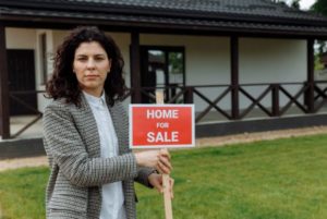 A woman holding a 'House For Sale' 