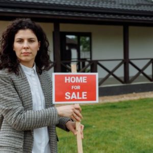 A woman holding a 'House For Sale'