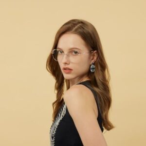 Portrait of a woman with light brown long hair, wearing glasses, a black top and large earrings on a yellow/beige background
